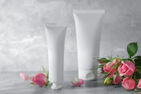 Tubes of hand cream and beautiful roses on light grey table