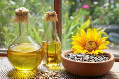 Bottles of sunflower oil, seeds and flower on wooden table indoors