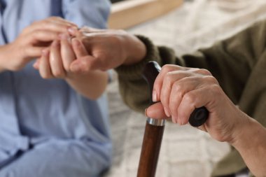 Caregiver and elderly woman with walking cane at home, closeup