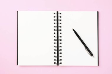 Soluk pembe arkaplandaki defter ve kalem, üst görünüm