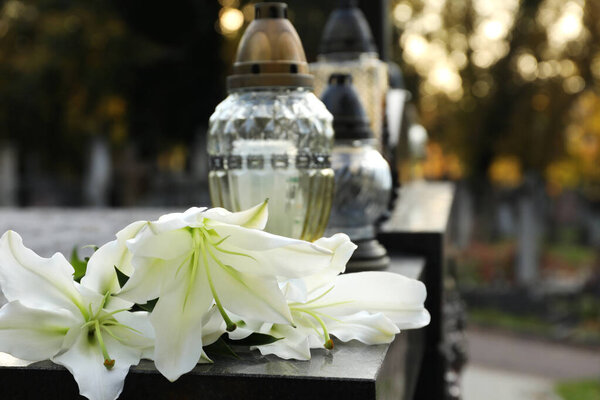 White lilies and grave lights on granite tombstone outdoors, space for text. Funeral ceremony