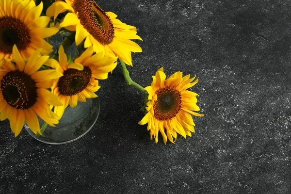 Glass vase with beautiful sunflowers on black table, above view. Space for text
