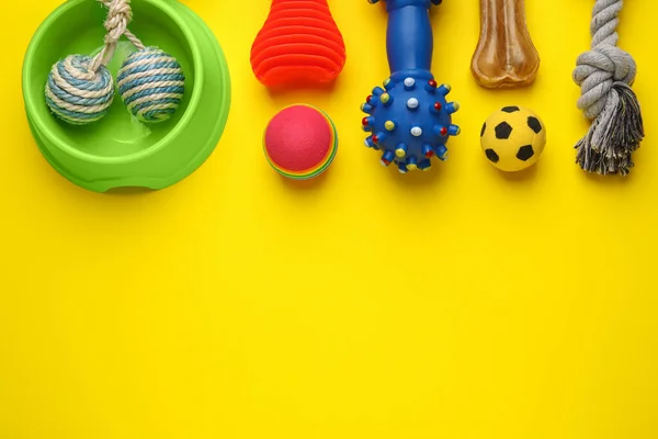 Flat lay composition with pet toys and feeding bowl on yellow background, space for text