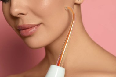 Woman using high frequency darsonval device on pink background, closeup