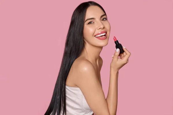 stock image Young woman with beautiful makeup holding glossy lipstick on pink background