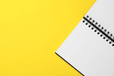 Blank notebook on yellow background, top view. Space for text