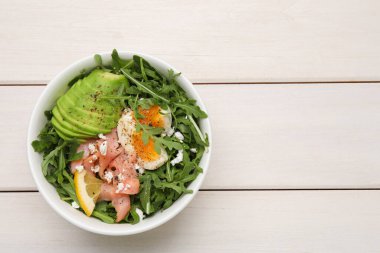 Haşlanmış yumurtalı lezzetli salata, somon balığı ve beyaz ahşap masada avokado, üst manzara. Metin için boşluk