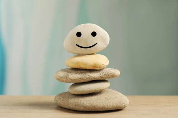 Stack of stones with drawn happy face on table against light turquoise background, closeup. Zen concept