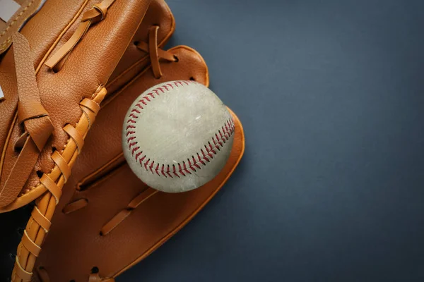 Catcher\'s mitt and worn baseball ball on dark background, top view. Space for text