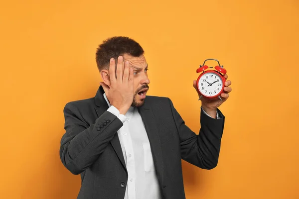 Emotional man with alarm clock on orange background. Being late concept