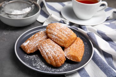 Gri masadaki pudra şekerli lezzetli madeleine kekleri.