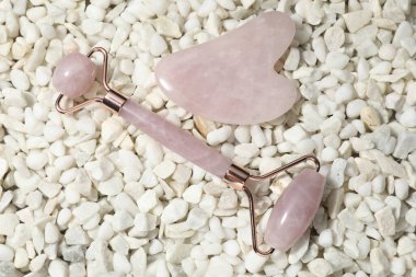 Quartz gua sha aracı ve beyaz taşlar üzerinde yüz yuvarlayıcı düz yatıyordu