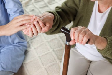 Caregiver and elderly woman with walking cane at home, closeup