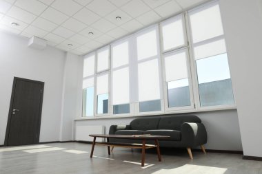 Rahat bir kanepe ve geniş pencerenin yanında beyaz jaluzili bir masa.