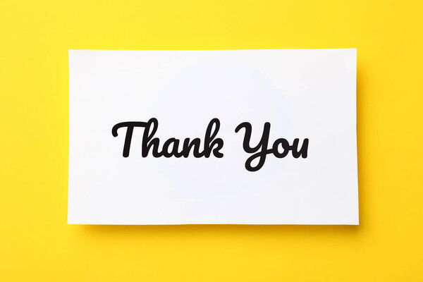 White paper note with phrase Thank You on yellow background, top view