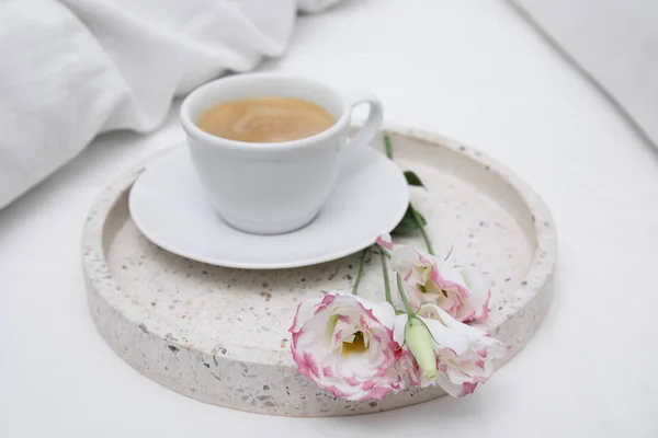 Tray with cup of coffee and flowers on white bed