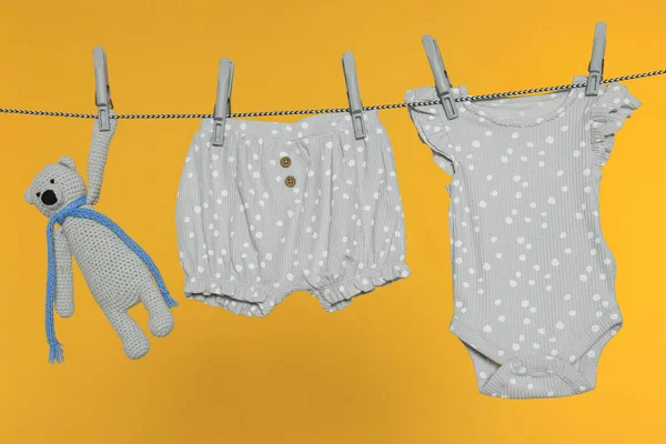 stock image Baby clothes and bear toy drying on laundry line against orange background