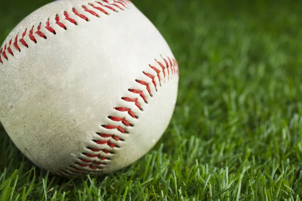 Worn baseball ball on green grass, closeup. Space for text