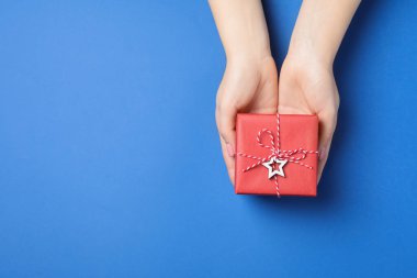 Mavi arka planda güzel paketlenmiş bir Noel hediyesi kutusu tutan bir kadın. Metin için boşluk