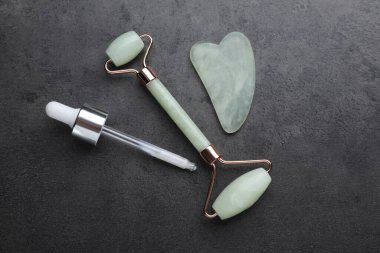 Quartz gua sha aracı, yüz silindirleri ve gri arka planda kozmetik ürünü ile damlatıcı, düz yatıyordu