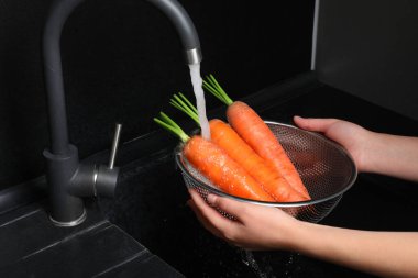 Woman washing fresh ripe juicy carrots under tap water in sink, closeup