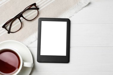 Bardakların yanında modern e-kitap okuyucusu ve beyaz ahşap masada bir fincan çay, düz bir şekilde yatıyordu. Metin için boşluk