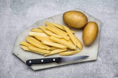 Açık gri masada bıçakla kesilmiş çiğ patatesler, üst manzara. Lezzetli patates kızartması.