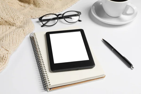 Modern e-book reader, notebook and pen on white table