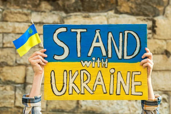 国旗と言葉の色でポスターを保持する女性レンガの壁に対してウクライナと屋外で立ちます クローズアップ — ストック写真