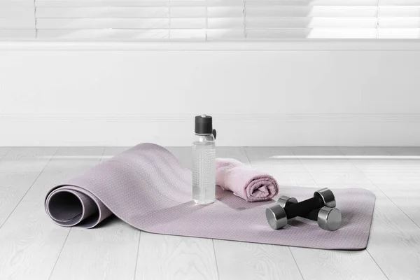 Exercise mat, dumbbells, towel and bottle of water on light wooden floor indoors