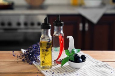Mutfaktaki ahşap masada farklı pişirme yağları, zeytinler, fesleğenler ve lavanta çiçekleri.