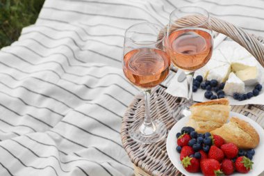 Glasses of delicious rose wine, food and basket on picnic blanket outdoors