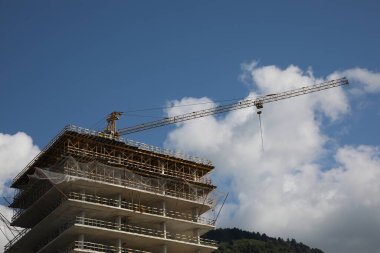 Mavi bulutlu gökyüzünün altındaki bitmemiş binanın üzerinde vinç kulesi olan inşaat alanı