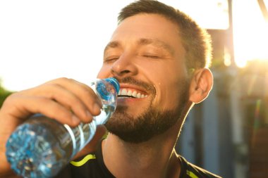 Happy man drinking water outdoors on hot summer day, closeup. Refreshing drink