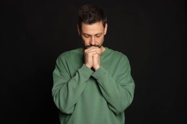 Elleri sıkıca bağlı siyah arka planda dua eden adam.