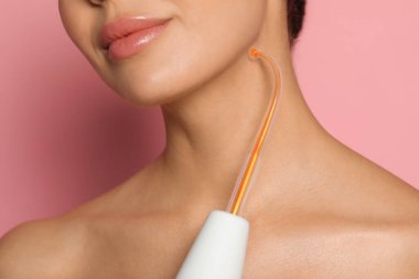 Woman using high frequency darsonval device on pink background, closeup