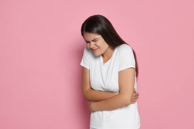 Pembe arka planda adet sancısı çeken genç bir kadın, mesaj için yer var.