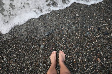 Çakıl taşlı plajda duran bir kadın güzel bir deniz dalgasının yanında, manzaralı.