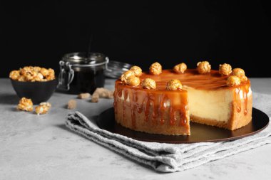 Sliced delicious cheesecake with caramel and popcorn on light grey table, space for text