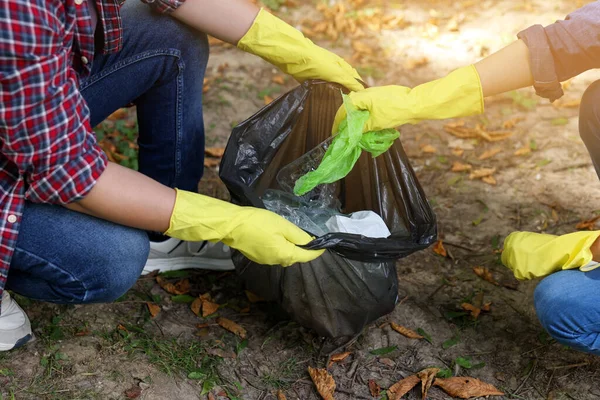 Man and woman with plastic bag collecting garbage in park, closeup