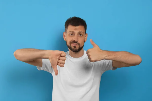 Man showing thumbs up and down on light blue background