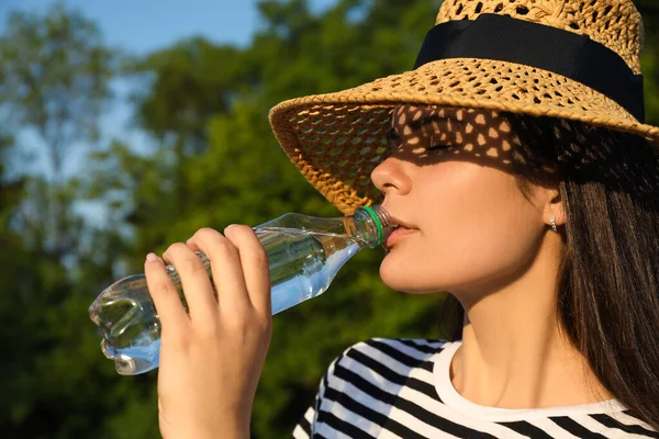 stock image Young woman in straw hat drinking water outdoors on hot summer day. Refreshing drink