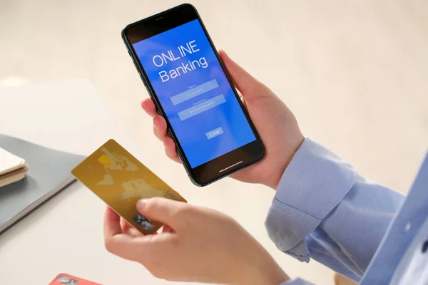スマートフォンでオンラインバンキングアプリを使用している女性とホワイトオフィステーブルでクレジットカード クローズアップ — ストック写真
