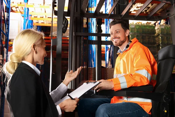 Happy worker talking with manager while sitting in forklift truck at warehouse