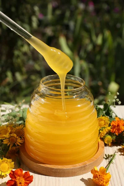 庭のテーブルの上に美しい花に囲まれたガラス瓶からのディップとおいしい新鮮な蜂蜜を取る — ストック写真