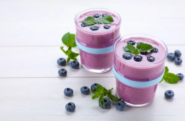 Glasses of blueberry smoothie with mint and fresh berries on white wooden table, space for text