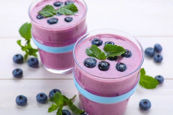 Glasses of blueberry smoothie with mint and fresh berries on white wooden table, closeup