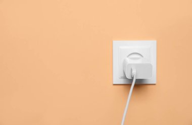 Şarj adaptörü soluk turuncu duvardaki güç prizine takılı, mesaj için yer var. Elektrik arzı