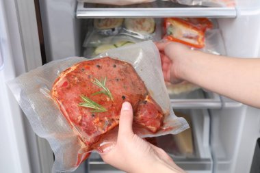 Woman putting vacuum bag with meat into fridge, closeup. Food storage clipart