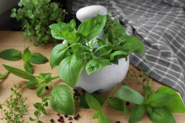 Farklı taze otlar ve ahşap masada siyah biberli havan topu, yakın plan.